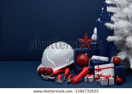Construction tools, hard hat, white fir tree, gift boxes and Christmas ornaments on dark blue background with copy space. New Year and Christmas construction background. For advertising or web design