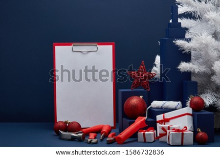 Construction tools, blank clipboard, white fir tree, gift boxes, Christmas ornaments on dark blue background with copy space. New Year, Christmas construction background. For advertising, web design