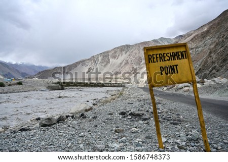 "REFRESHMENT POINT" sign on the road in Ladakh, India.This sign is made of yellow painted wood.Traffic sign with mountain and blue sky background.