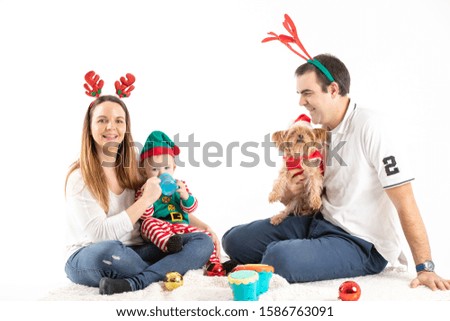 Stock studio photo of a couple with a baby and a dog sitting on the floor dressed in Christmas elements with a white background.