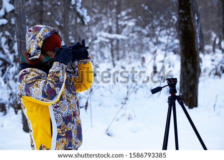 The girl with the camera and a support on a winter landscape. The photographer shoots interesting scenes in the forest. Snow, frosty air. The freelancer works. Sphere of employment.