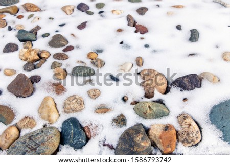 Snow lies on a stone shore. Background of stones and fresh snow. Winter concept