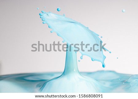 Baby blue colored milk splashes into water and is frozen in space with high speed photography
