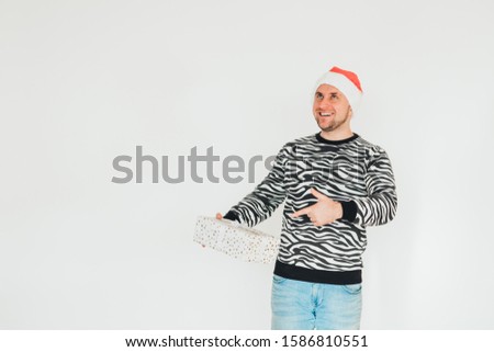 Presents gift box. Santa man holds gift. Bearded man in Santa hat shows with finger on gift box. Stylish man with presents gift box. New year, winter, Christmas presents. Discount, sale, season sales