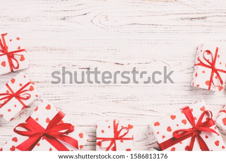 Valentine or other holiday handmade present in paper with red hearts and gifts box in holiday wrapper. Present box of gift on white wooden table top view with copy space, empty space for design.