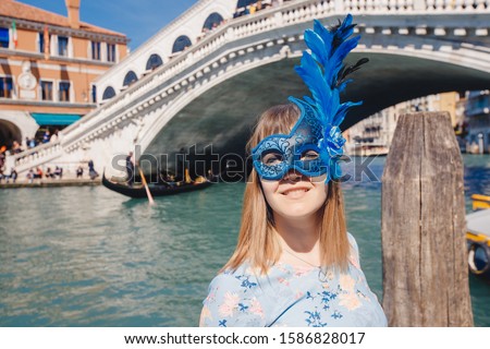 Portrait smiling young woman in Venice in Venetian blue mask against backdrop of great canal and bridge. Concept travel.