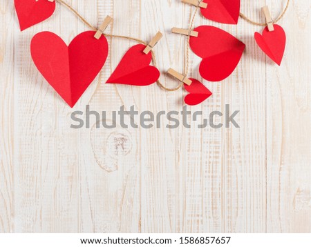 The concept of the preparation for Valentine's Day. Red hearts are held by clothespins on a jute rope, on a white wooden background. Copy space.