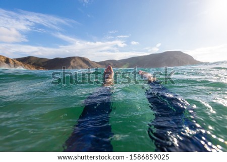 A picture of feet in the sea with rocky mountains on the background under a blue sky in Portugal