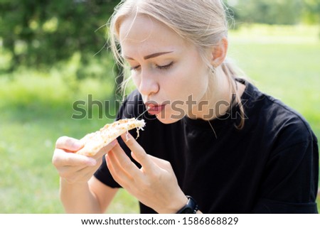 Beautiful girl eating trying tasting pizza outdoor in park