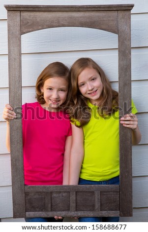 Twin sister girls posing with aged wooden border frame on white wall