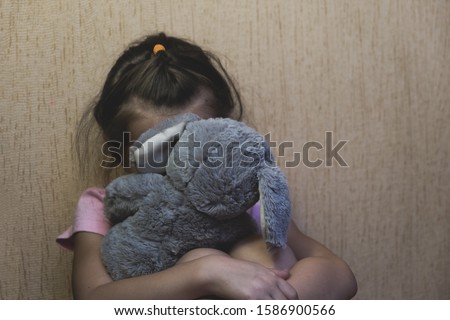 Depressed child sitting and hidden behind her toy teddy bear. domestic and violence, beaten sitting at the wall, Domestic violence. Copy space. Royalty-Free Stock Photo #1586900566