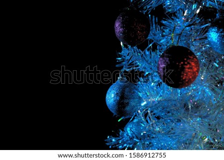 Close-up of shiny white and red balls hanging on a silver artificial Christmas tree in the rays of blue lighting on a black background, selective focus and place for text .