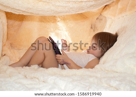 Little girl with an internet tablet under the covers. Baby girl of two years old is using digital tablet and playing in bed instead of sleeping