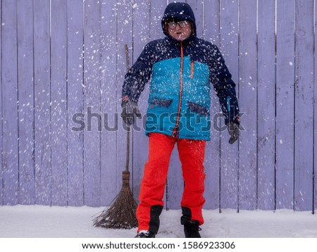 man in bright ski suit stands holding broom in his hands and is going to clean the snow in winter yard