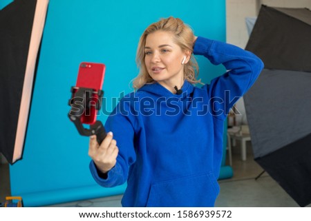 Attractive woman blogger shoots video on smartphone in studio.