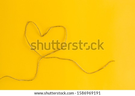 A thread in the shape of the heart on yellow background. Flat lay style. Top view