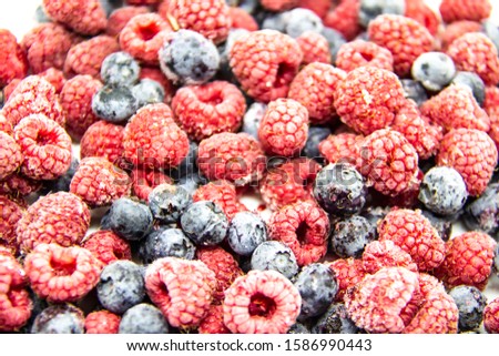 A Berry mix from frozen raspberries and blueberries. A Frozen Berries from freezer.  A sweet background with frozen raspberries and blueberries.   A heathy Berries in the background. 