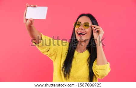 Smiley girl. Close-up photo of a charming young lady, who is taking a selfie in a yellow knitted sweater and sunglasses, which she is touching with her fingers.