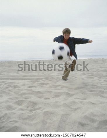 View of a young boy playing with a soccer ball on a beach