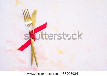 Golden cutlery in red ribbon on a pink background . Spring holidays cooking and celebration concept. Top view, flat lay, copy space.
