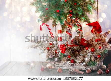 Christmas background with wicker basket, Santa Claus boot, hat, candle, star, fir tree, candy cane lollipop on table, New Year winter holiday home natural material decor, glowing festive bokeh.