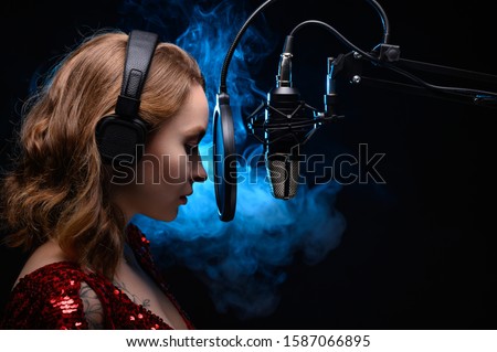 A girl singer sings into a microphone, with a spectacular background, vocals, a recording studio, recording a track. On a black background, with a blue backlight. Vocal school, and training