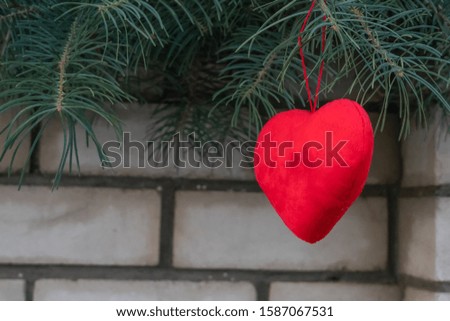 red heart hangs on a spruce tree on the street against a brick white wall. Copy space. concept of the outdoor festival.