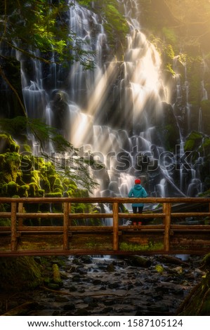 Hiker on wooden bridge look at waterfall, Ramona Falls, Oregon. Sunbeam cross over waterfall and touch on moss