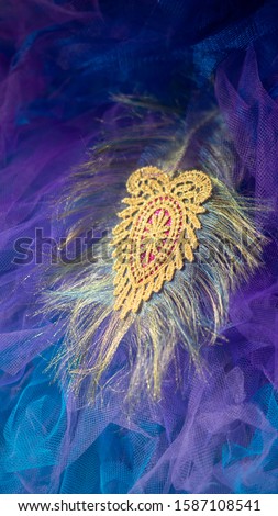 Textile art  gold peacock feather with purple and blue tulle fabric background