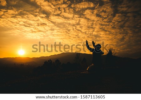 Pray of man kneeling down and lift hands at sunset background. christian silhouette concept.