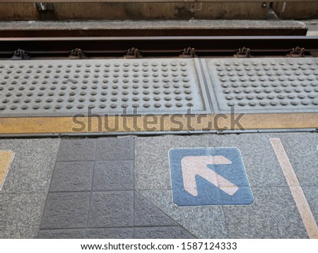 yellow arrow sign on floor platform at skytrain station.