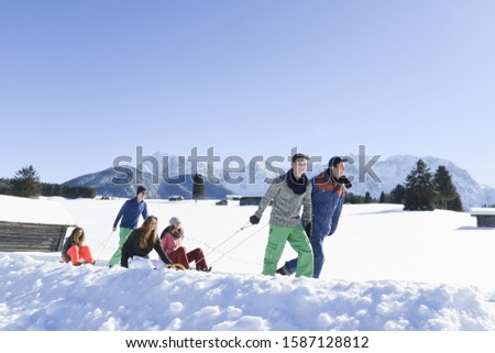 Young friends pulling girls friends on sleds through snow