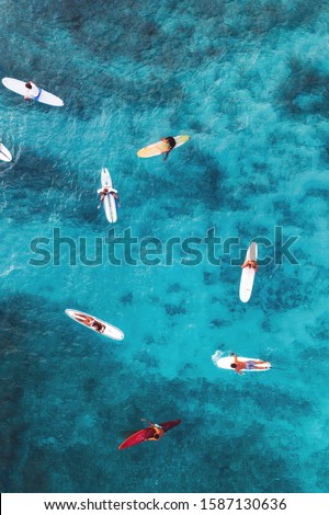 Aerial pic of surfers seating on surfboards and waiting for wave in the middle of ocean with perfect weather and clean water at sunset time in Hawaii paradise, shot on drone from above