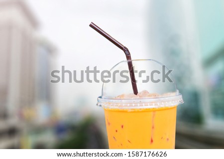 Picture of a half plastic cup of Thai tea, blurry cityscape for background