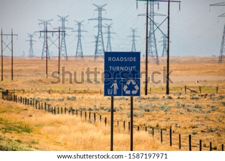 Information Road blue Sign, Roadside turnout with Tidy man and Recycling symbols against yellow prairies and plains and electrical lattices background