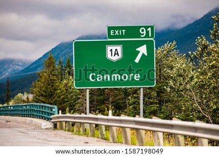 Information road green sign, the next exit after 91 km, Canmore, 1A road symbol, Canadian rural roadside forests in the background, Alberta, Canada