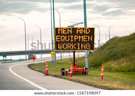 Temporary condition Variable message sign with orange barrels on the right roadside Men and equipment working, work zone on the Canadian highway roads