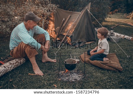 Grandfather and his grand child are camping, talking and eating canned  food. Image with selective focus and toning