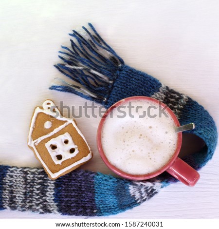 gingerbread house and a mug of cappuccino on a table with a scarf top view. cozy winter coffee house