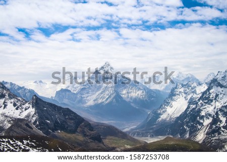 Ama Dablam mountain rises above valley in cloudy day near Cho La pass in Sagarmatha national park in Himalayas. Ghola Tsho lake is visible at the foot  of mountain.