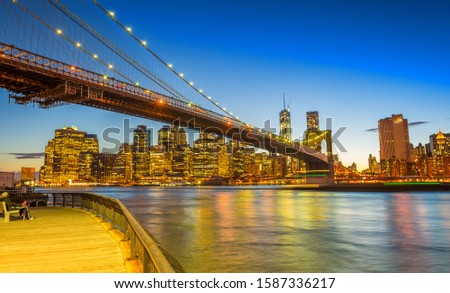 Amazing Manhattan skyline and Brooklyn Bridge after sunset with river reflections.