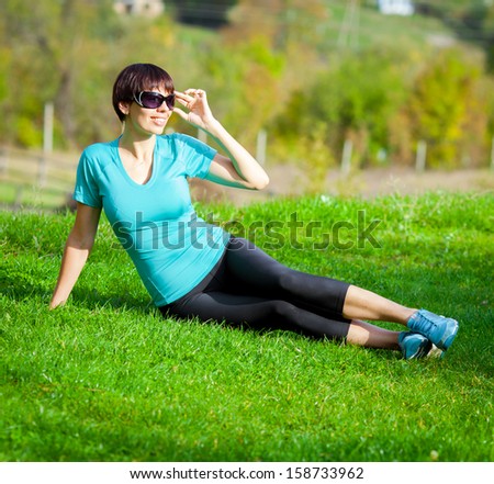 Young beautiful sporty woman sitting on green grass