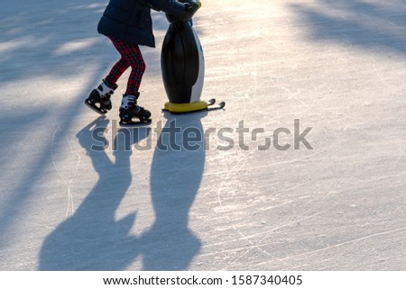 A child learns to skate on an ice rink and holds on to a plastic penguin for support.Winter time, family activities and sport concept. Christmas holidays, fun on a frosty day for kids. copy space