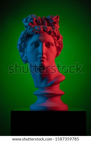 Plaster statue bust of Apollo Belvedere in red and blue light on a green background
