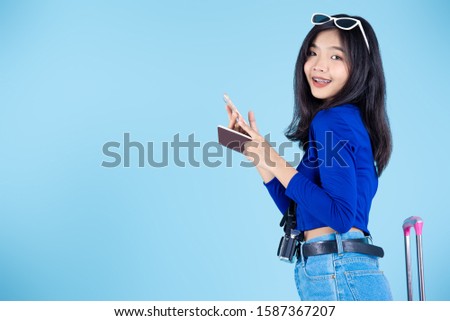 Asian tourist with pink luggage holding passport and smart phone on blue background.