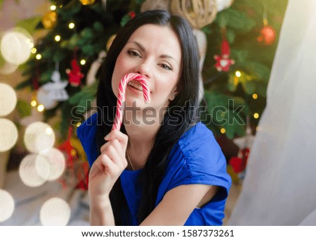 Happy mom and daughter kiss and hug near the Christmas tree. New Year and Christmas concept. Mom brunette in a blue dress and a daughter with pigtails, dressed in a checkered dress.