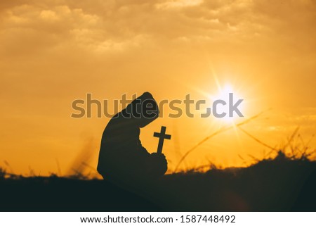 Man sit down and praying with holding the cross in hand at sunset background. christian silhouette concept.