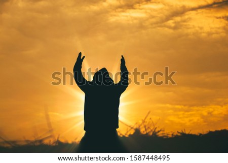 Man raise two hands to sky for praying to God at sunset background. christian silhouette concept.