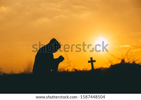 Man kneeling down and praying with the cross at sunset background. christian silhouette concept.