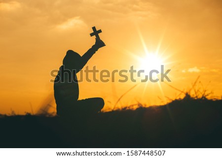 Man sit down and praying with raise the cross to sky at sunset background. christian silhouette concept.